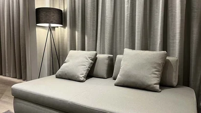 Divano grigio con cuscini davanti a tende e lampada da terra nera