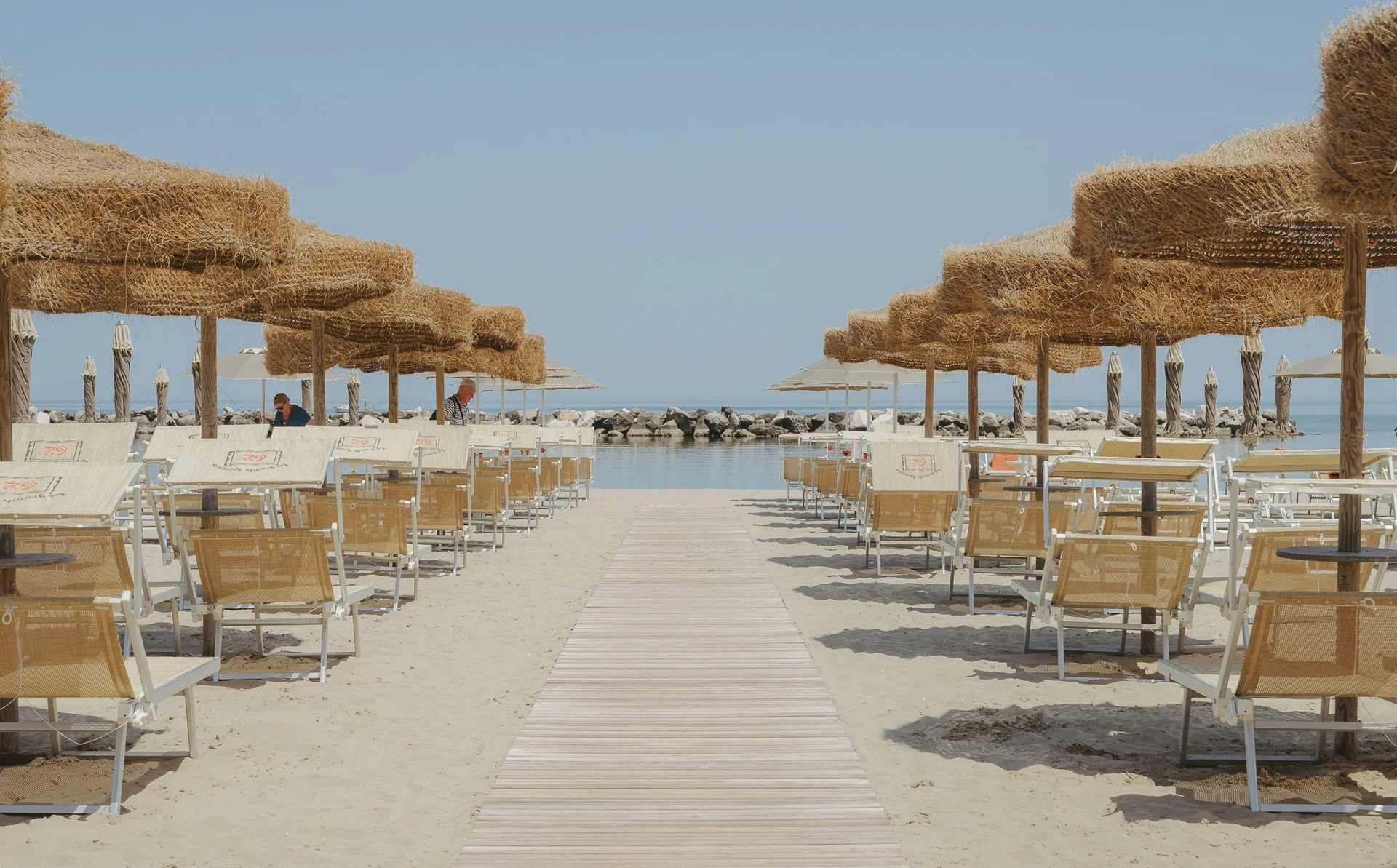 Evangelisti Palace. Residence di lusso a Bellaria-Igea Marina. Ombrelloni di paglia e sedie a sdraio ordinate su una spiaggia sabbiosa