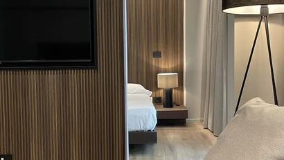 Interno moderno con divano beige, lampada a treppiede e camera da letto dietro