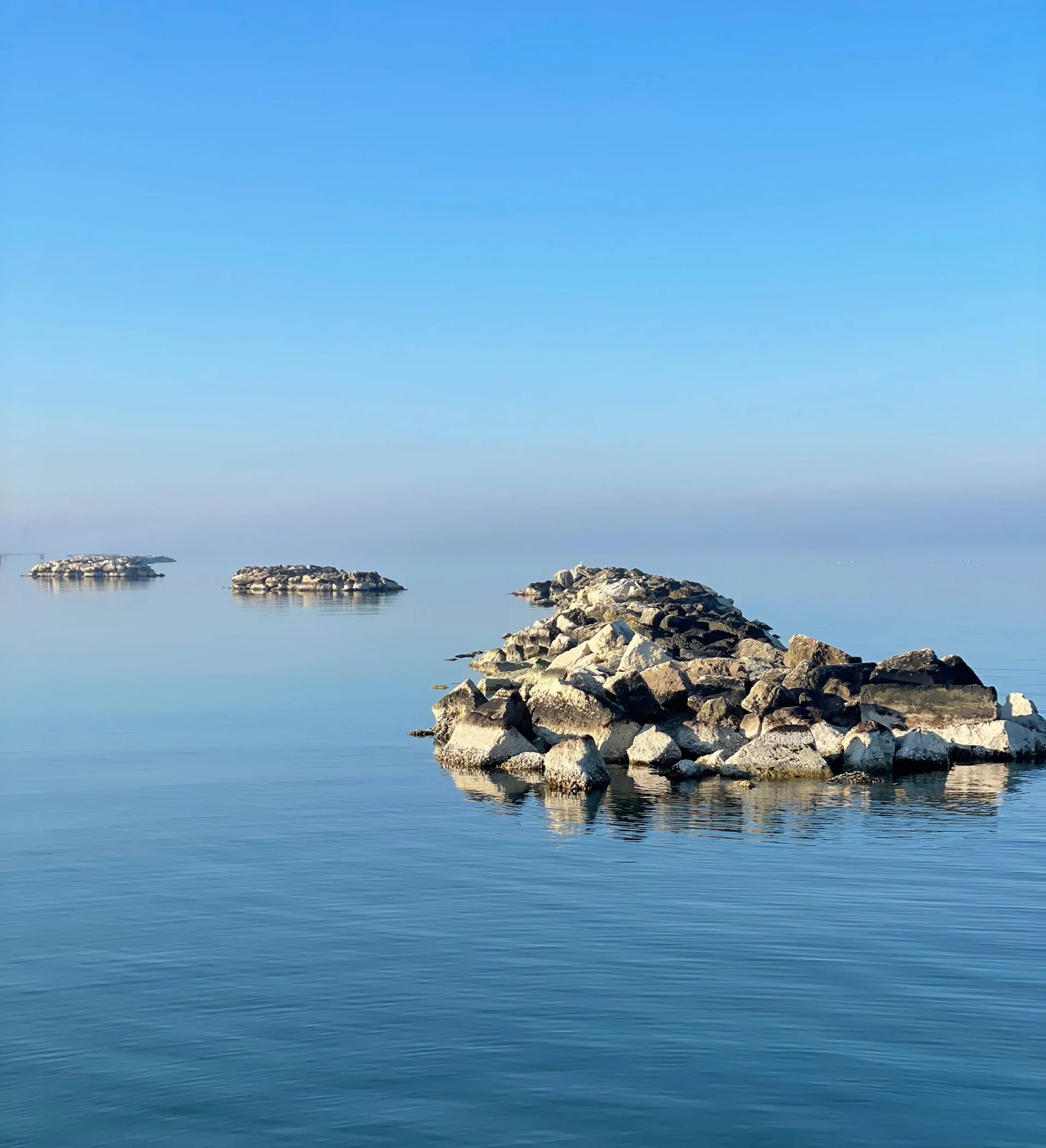 Scogliera di rocce che si estende nell'acqua calma sotto un cielo limpido