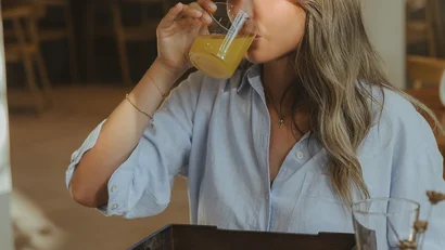 Donna che beve succo d'arancia a colazione con vari piatti sul tavolo