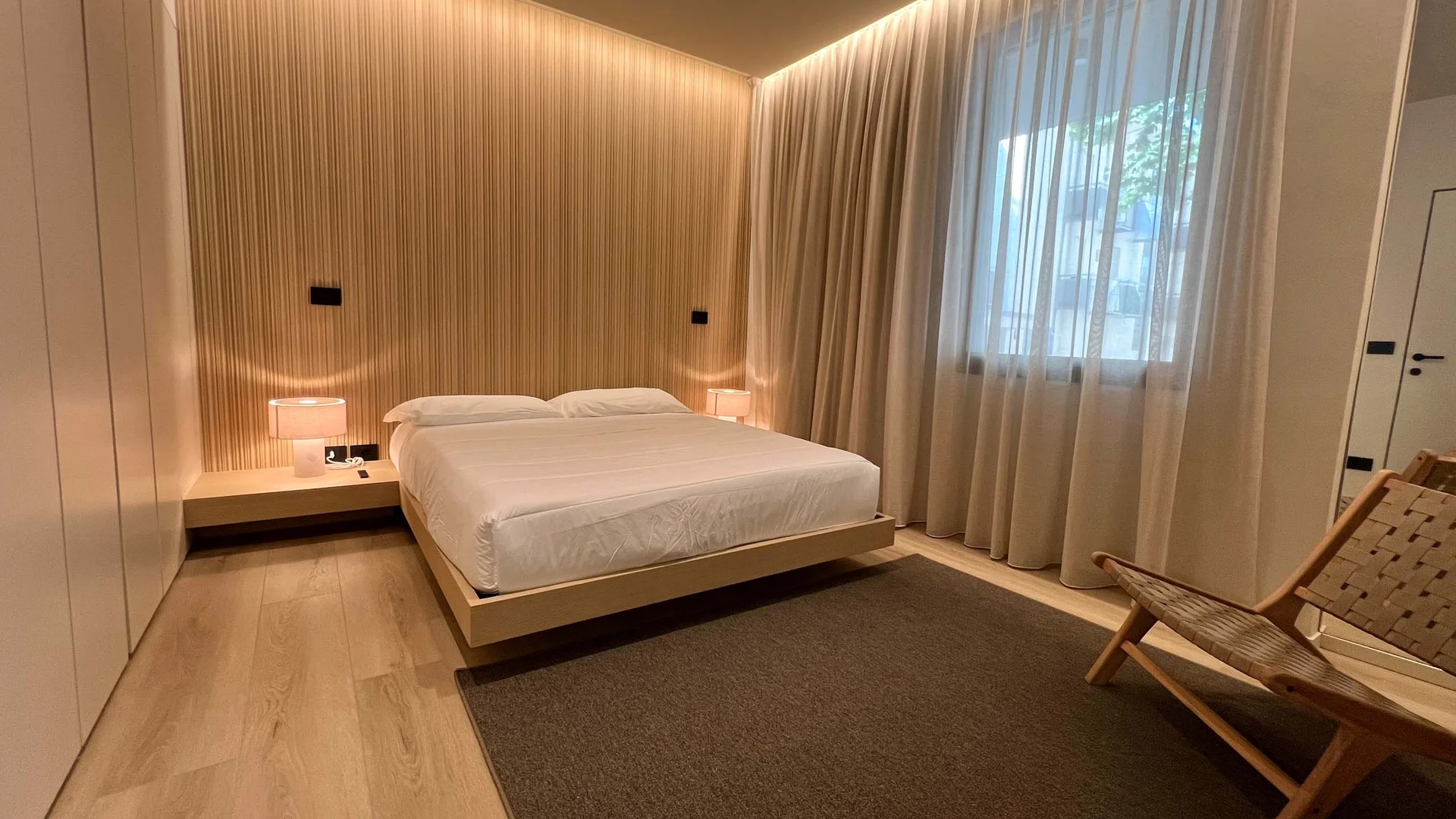 Camera da letto moderna con letto matrimoniale, lampade e sedia in legno